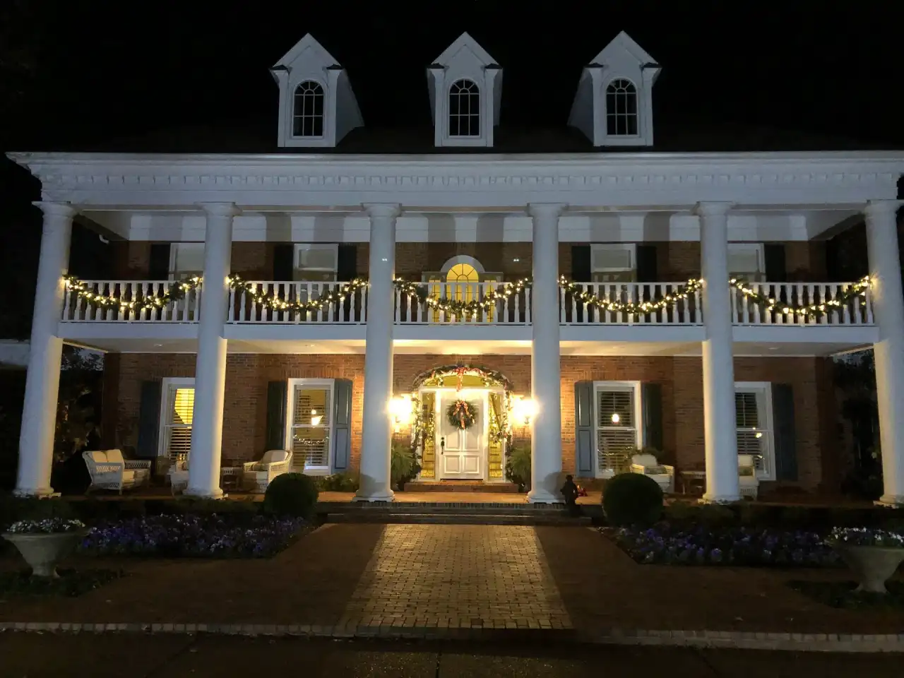 Colonial home with white columns, lit garland on the balcony rails and a lit wreath on the front door