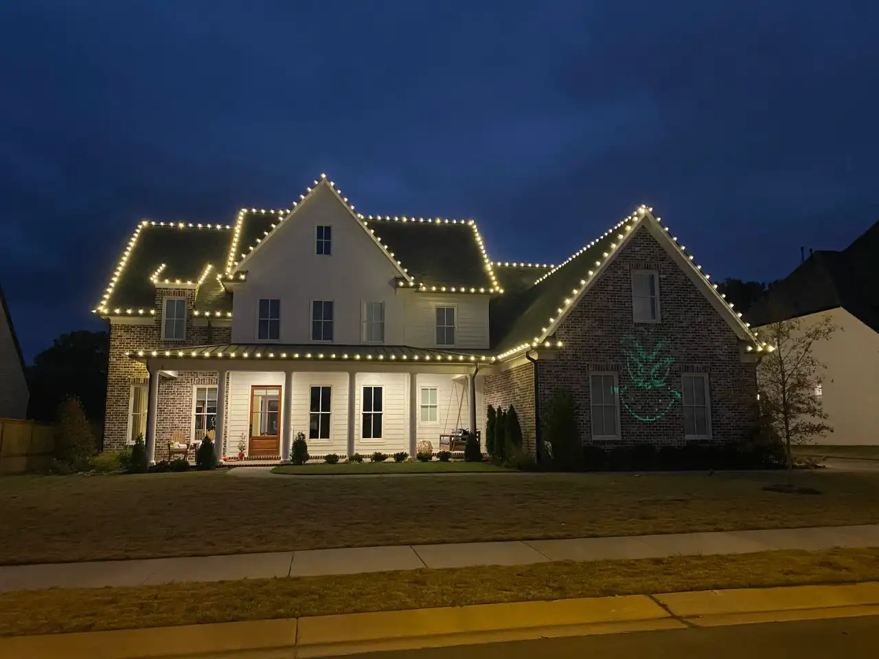 Two-story farmhouse with warm white C9 lights outlining the roofline at dusk